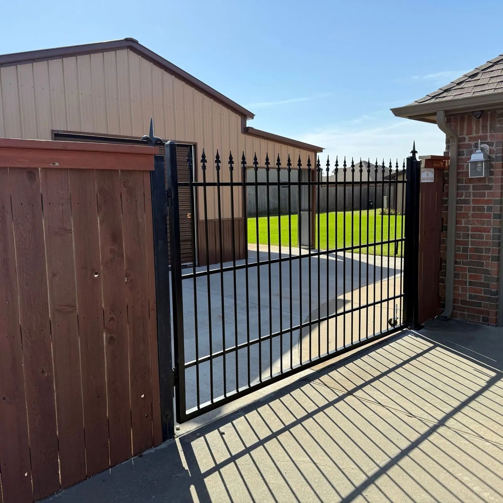 Black wrought-iron driveway gate beside a cedar wood privacy fence